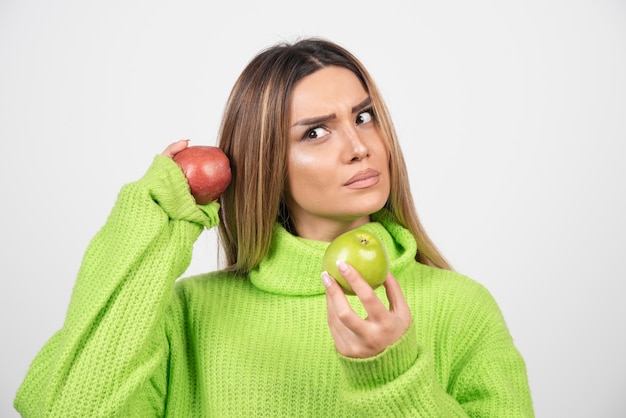 Mujer joven en camiseta verde sosteniendo dos manzanas arriba.
