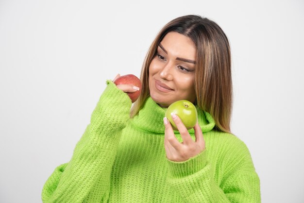 Mujer joven en camiseta verde sosteniendo dos manzanas arriba