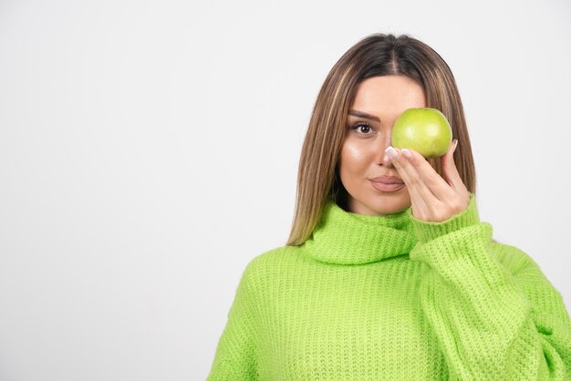 Mujer joven en camiseta verde sosteniendo una manzana.