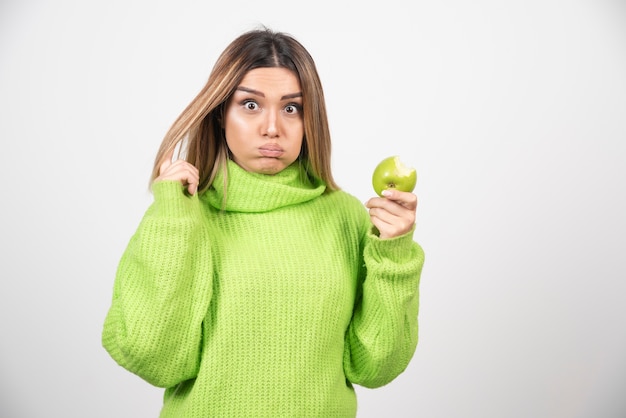 Mujer joven en camiseta verde sosteniendo una manzana.