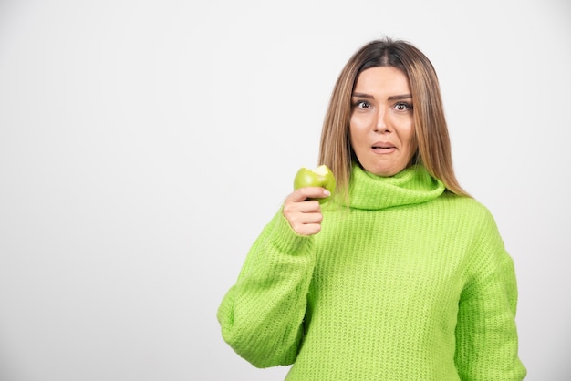 Mujer joven en camiseta verde sosteniendo una manzana.