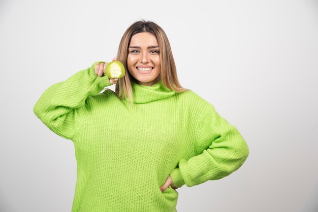 Mujer joven en camiseta verde sosteniendo una manzana.