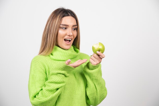 Mujer joven en camiseta verde sosteniendo una manzana.