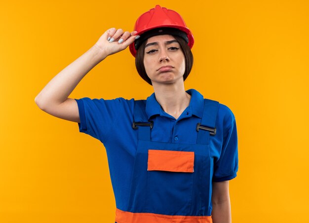 Mujer joven cansada del constructor en uniforme que sostiene el casco de seguridad