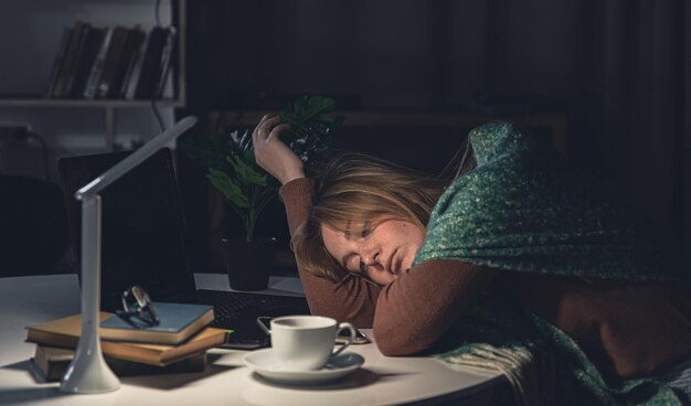 Mujer joven cansada en el lugar de trabajo quiere dormir hasta tarde en la noche