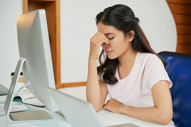 Mujer joven cansada a la mesa en la oficina