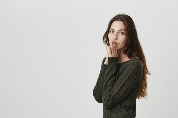 Mujer joven cansada y preocupada suplicando, cogidos de la mano cerca de los labios esperanzados