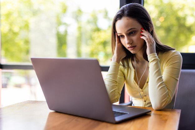 Mujer joven cansada que trabaja en la computadora portátil en su espacio de trabajo