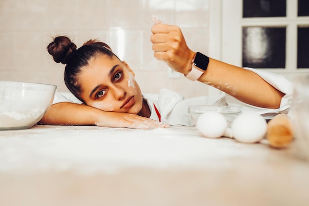 Foto gratuita mujer joven cansada está vertiendo harina en la mesa de la cocina