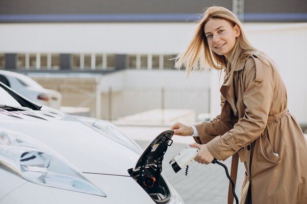 Mujer joven cargando su coche eléctrico con pistola de carga