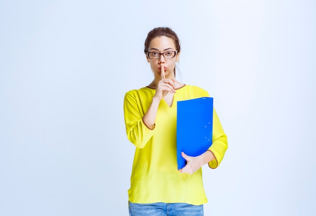 Foto gratuita mujer joven con una carpeta azul pidiendo silencio