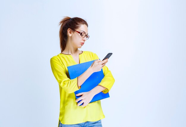 Mujer joven con carpeta azul revisando sus mensajes