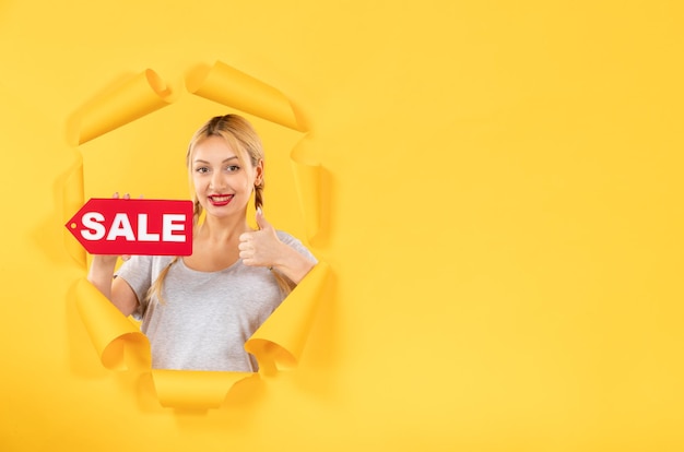 Foto gratuita mujer joven con cartel de inscripción de venta en compras interiores de fondo de papel amarillo rasgado