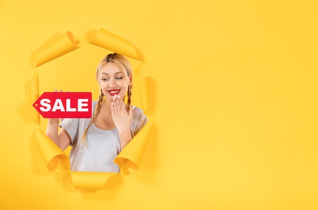 Mujer joven con cartel de inscripción de venta sobre fondo de papel amarillo rasgado compras interiores faciales