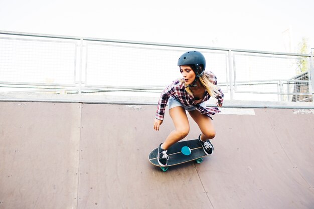 Mujer joven con casco patinando en el half pipe