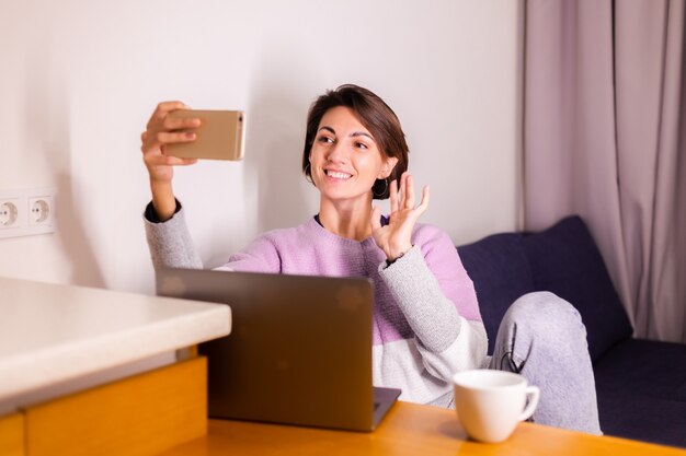 Mujer joven caucásica en el dormitorio en el sofá mira la cámara del teléfono móvil