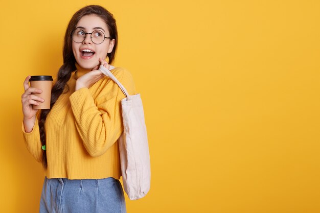 Mujer joven caucásica emocionada con expresión facial feliz, hacer compras en el centro comercial y beber café para llevar. Copie espacio para publicidad o texto promocional.