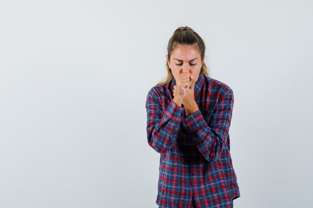 Mujer joven caughing en camisa a cuadros y mirando agotado