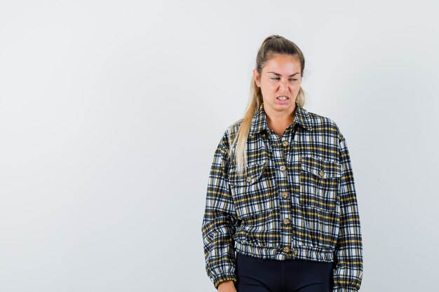 Mujer joven con el ceño fruncido en camisa, pantalones cortos y mirando insatisfecho, vista frontal.