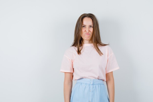 Mujer joven con el ceño fruncido en camiseta, falda y mirando disgustado. vista frontal.