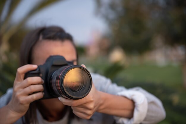 Mujer joven de cerca tomando fotografías al aire libre con una cámara SLR profesional.