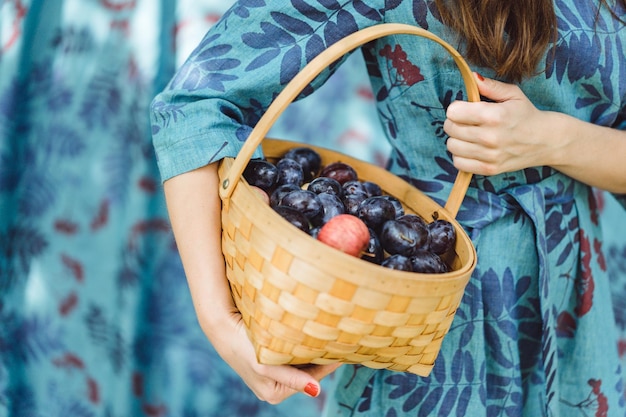Mujer joven con una cesta de frutas, ciruelas y manzanas.