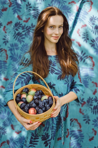 Mujer joven con una cesta de frutas, ciruelas y manzanas.