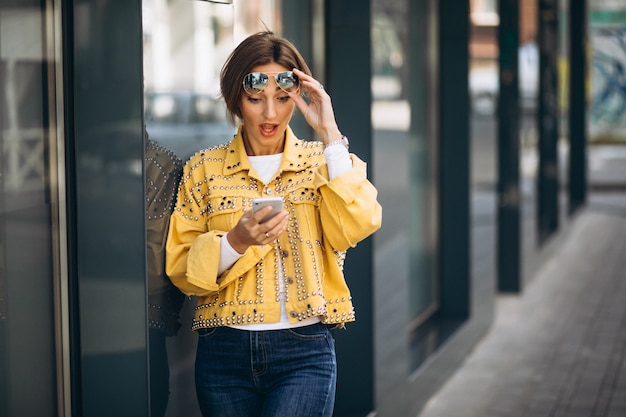 Mujer joven en chaqueta amarilla con teléfono afuera en la calle