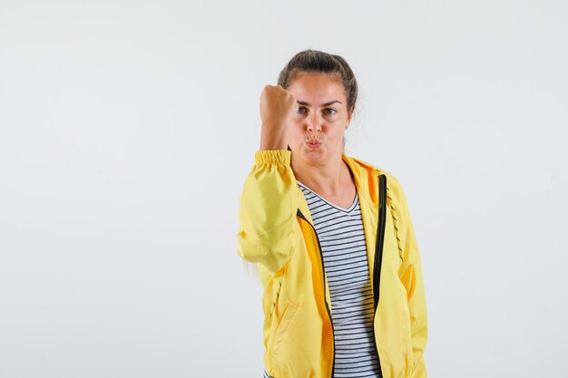 Mujer joven con chaqueta, camiseta mostrando el puño cerrado y mirando confiado, vista frontal.