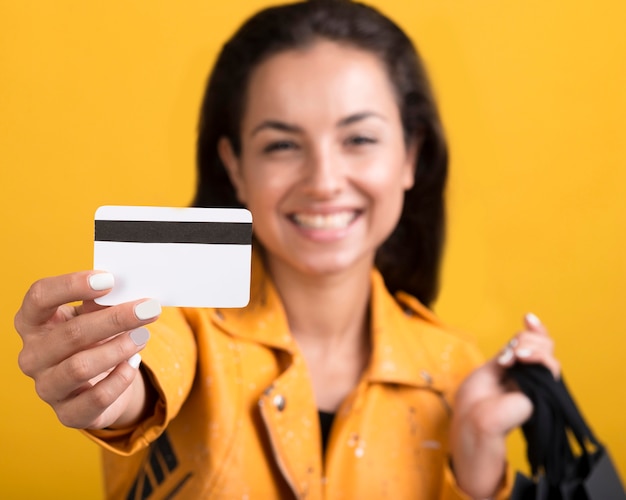 Mujer joven en chaqueta de cuero amarilla mostrando tarjeta de compras