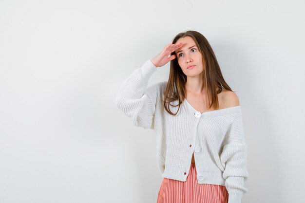 Mujer joven en chaqueta de punto y falda mirando lejos con las manos sobre la cabeza aislado