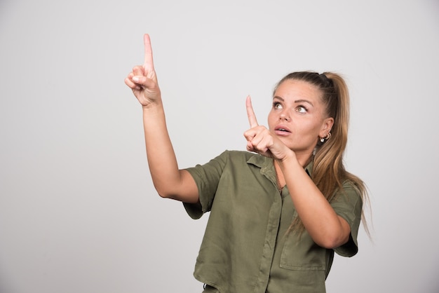 Foto gratuita mujer joven con chaqueta verde apuntando a su lado.