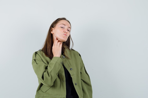 Mujer joven en chaqueta verde mientras envía beso, vista frontal.