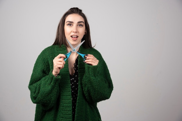 Mujer joven con chaqueta verde mostrando unas tijeras.