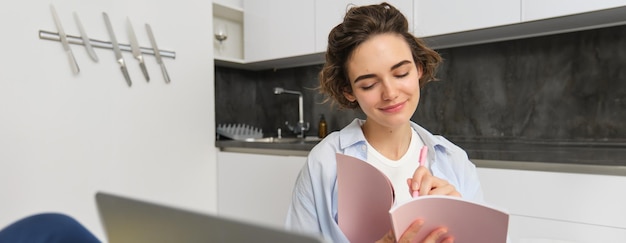 Foto gratuita mujer joven chequeando su horario mientras trabaja remotamente desde casa usando una computadora portátil mirándola