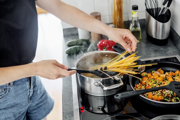 Mujer joven cocinando pasta de espagueti fresco en casa con verduras.