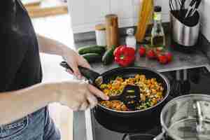 Foto gratuita mujer joven cocinando verduras frescas en una sartén en casa.