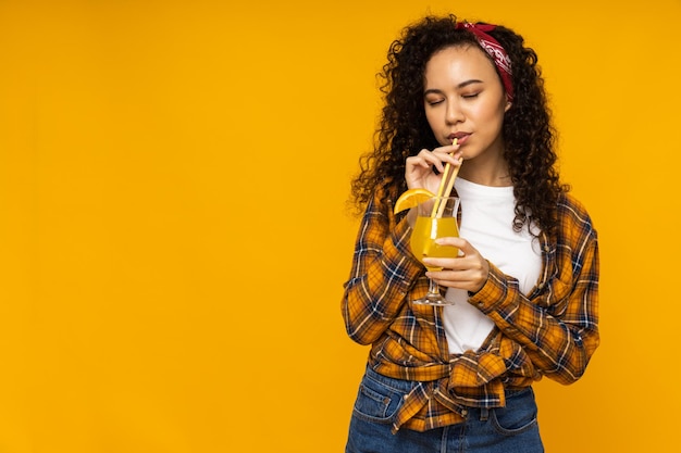 Mujer joven con cóctel sobre fondo amarillo