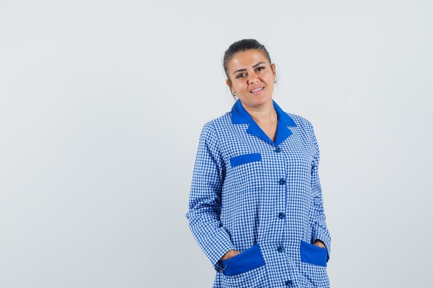 Mujer joven cogidos de la mano en los bolsillos en camisa de pijama de cuadros azules y luciendo bonita. vista frontal.