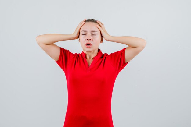 Mujer joven cogidos de la mano a la cabeza en camiseta roja y mirando con cuidado