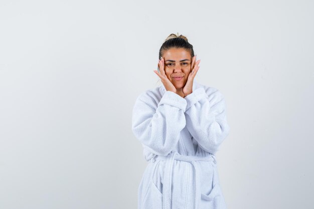 Mujer joven cogidos de la mano en las mejillas en bata de baño y mirando confiado