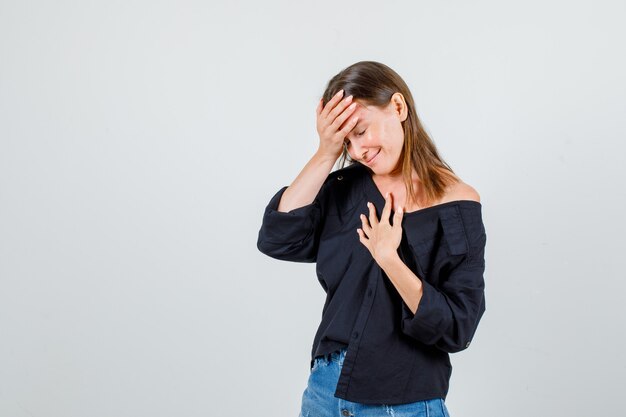 Mujer joven cogidos de la mano en el pecho y la frente en camisa, vista frontal de pantalones cortos.