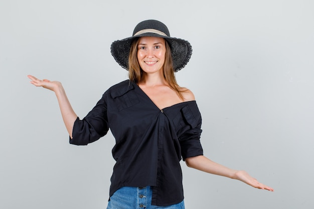 Mujer joven cogidos de la mano para recuperar el equilibrio en camisa, pantalones cortos, sombrero y mirando alegre. vista frontal.