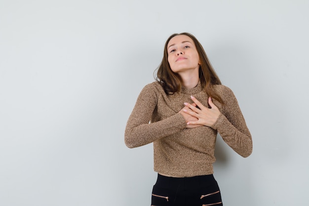 Mujer joven cogidos de la mano en su corazón en blusa dorada y mirando deseoso