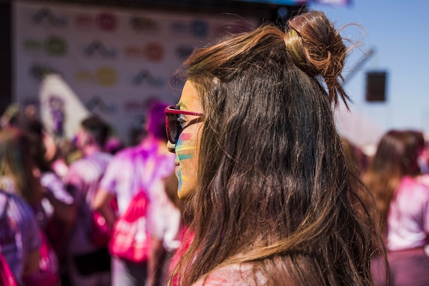 Mujer joven con color pintado de holi en su cara mirando a otro lado