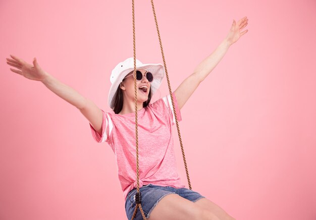 Mujer joven en un columpio sobre un fondo rosa.