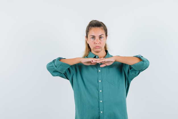 Foto gratuita mujer joven combinando sus manos sobre su pecho con camisa azul y mirando seria