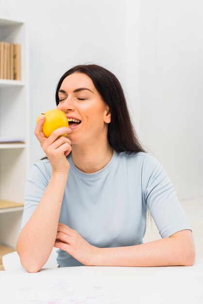 Mujer joven, comer, manzana amarilla, en la mesa