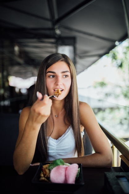 Mujer joven comiendo comida saludable sentado en el hermoso interior