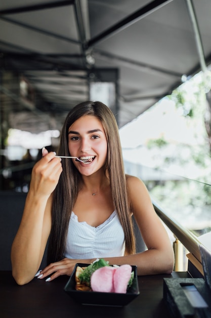 Mujer joven comiendo comida saludable sentado en el hermoso interior